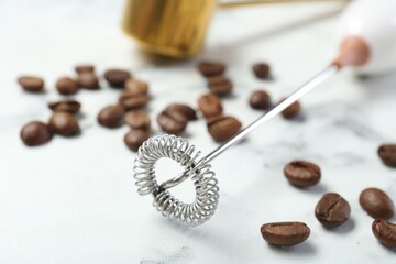 Milk frother wand and coffee beans on white marble table, closeup