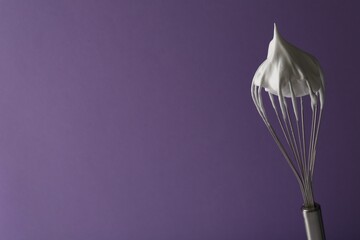 Whisk with whipped cream on violet background. Space for text