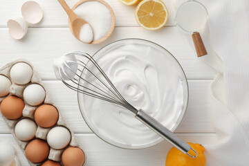Bowl with whipped cream, whisk and ingredients on white wooden table, flat lay