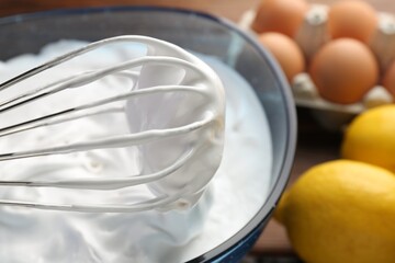 Bowl with whipped cream, whisk and ingredients on table, closeup