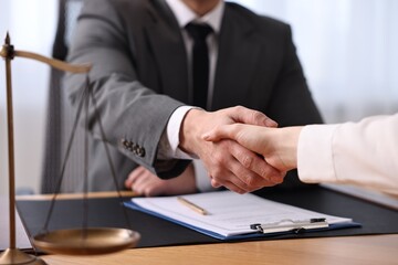 Notary shaking hands with client at wooden table in office, closeup