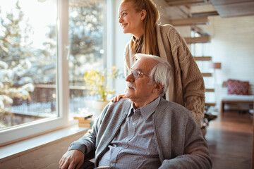 Young woman caring for elderly man in a sunlit room with winter scenery outside