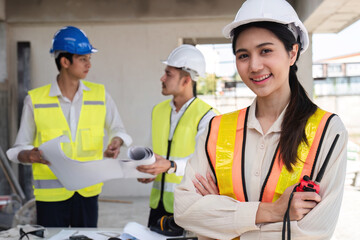 Portrait of a young Asian engineer standing with her arms crossed at a construction site. Portrait of successful young female engineer standing, smiling and looking at camera in engineer's uniform