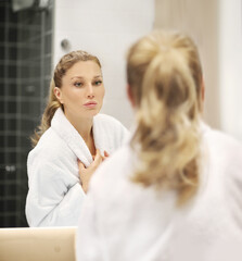woman looking in the mirror in the bathroom and taking care of her skin.