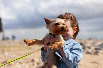 Little girl with a Yorkshire Terrier dog on a walk on the beach