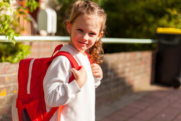 Cute schoolgirl with red backpack going to school on a sunny day