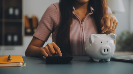 Young Asian woman saving for retirement Saving money through a piggy bank and taking notes on notebook, savings concept. - obrazy, fototapety, plakaty