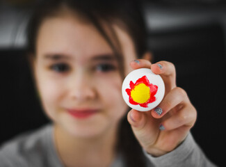 Little caucasian girl in a gray turtleneck shows an Easter egg with a red-yellow acrylic paint