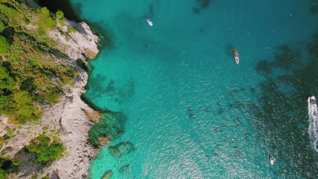 A stunning top down view of boats floating on clear turquoise sea waters near rugged cliffs. Capri Island, Italy.