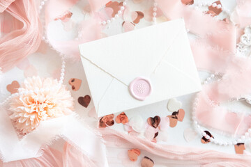 Sealed envelope near pink decorations, hearts and silk ribbons on white table top view, mockup