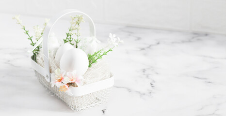 Decorative white eggs in a metal basket with eggs, spring flowers and straw on a marble table .