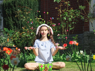 Portrait of a caucasian teenage girl throwing Easter chocolate eggs while sitting on the lawn.