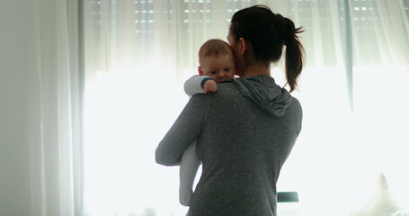 Real life mother holding newborn baby at home next to curtain window