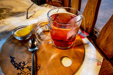Glass of rosehip tea, tea bag, lemon, honey, spoon on wooden pad. - 736427939