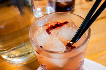 Cocktail with black straw, gin, pomegranate seed and ice cube on table. - 736428103