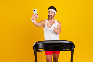 Photo of funny excited guy activewear walking treadmill showing finger apple iphone samsung modern gadget isolated yellow color background