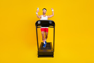 Full length photo of strong funny guy sportswear running treadmill rising fist tacking selfie...