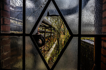 Aufnahme von Rohren und Bäumen durch ein zerbrochenes rautenförmiges Fenster in einem alten...