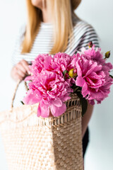 Beauty fashion closeup with women's hands holing a straw bag with peonies .Peony summer flowers bouquet. Lifestyle photo wuth flowers and a copy space.