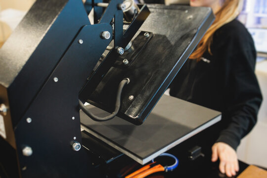 Process of printing image on clothes, heat press machine printing custom design on t-shirt and hoodie in fabric workshop, screen printing shirt, textiles and clothing, lithography and serigraphy