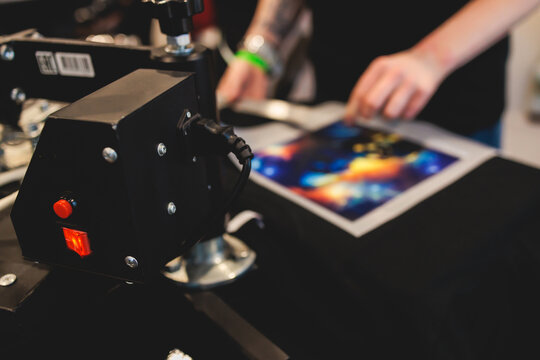 Process of printing image on clothes, heat press machine printing custom design on t-shirt and hoodie in fabric workshop, screen printing shirt, textiles and clothing, lithography and serigraphy