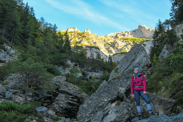 Fototapeta premium Hiker woman with panoramic view of majestic mountain peak Foelzstein in untamed Hochschwab mountain region, Styria, Austria. Scenic hiking trail on in remote Austrian Alps. Wanderlust in alpine summer