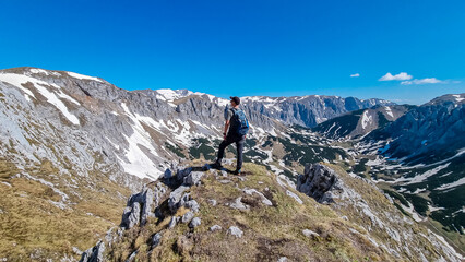 Hiker man with panoramic view of majestic mountain peak Ringkamp in wild Hochschwab massif, Styria, Austria. Scenic hiking trail in remote Austrian Alps on sunny day. Wanderlust in alpine spring