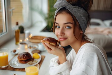A content woman savors her breakfast, biting into a delicious sandwich while enjoying a refreshing orange juice, surrounded by the warm and cozy ambiance of her indoor space