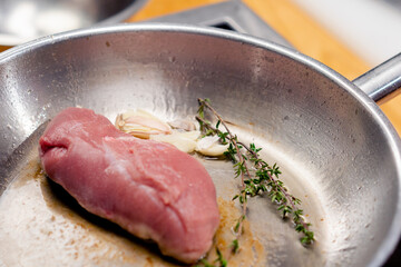 close-up of a piece of pink duck breast with rosemary on hot frying pan starting to fry