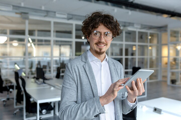Smiling young professional with curly hair using a digital tablet in a bright contemporary office setting, exemplifying modern worklife.