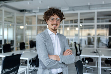 Portrait of a young mature male professional with curly hair confidently standing in a well-lit corporate office.