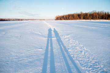 A persons shadow falls on the calm, freezing snowy field under the azure sky