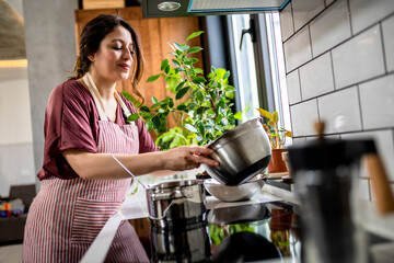 Latino woman cooking in her modern kitchen stirring in pot making food for dinner.