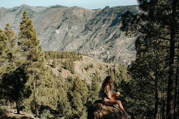 Turystka siedzi na kamieniu w cieniu na tle gór, Gran Canaria, Hiszpania - obrazy, fototapety, plakaty