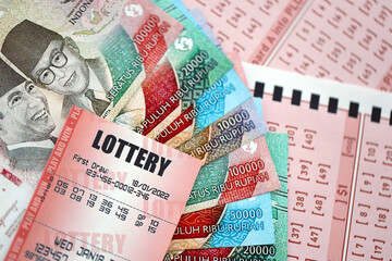 Red lottery ticket lies on pink gambling sheets with indonesian rupiah money bills. Lottery playing concept or gambling addiction in indonesia
