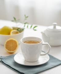 A cup of tea with lemon and a teapot on a white table against the background of a kitchen window close up.