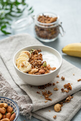 Homemade granola with banana and nuts in a bowl on a blue background with dry crynchy and branch.
