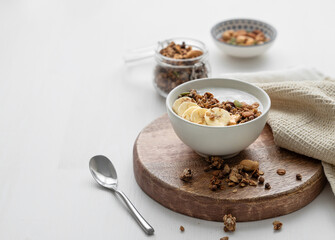 Baked granola with yogurt and banana on a cutting board on a white table.