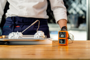 close-up of a chef in a white uniform in the kitchen at the table getting ready check the temperature of the product