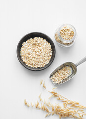 Oatmeal in a plate, jar and in a scoop on a white textured background with dry branch.
