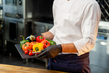 close-up of a chef holding a tray with different washed vegetables ready use colorful vegetables in...