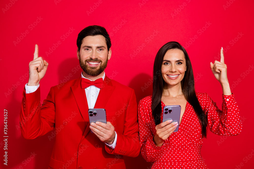 Poster portrait of two cheerful elegant people toothy smile hold smart phone direct finger up empty space i
