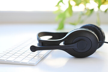 Headset with microphone and keyboard, placed on a white desk. Bright background light streaming in...