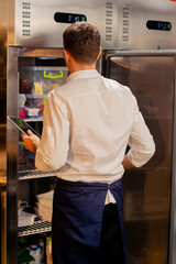 Fototapeta na wymiar professional kitchen chef looks into the fridge and chooses ingredients for cooking food concept