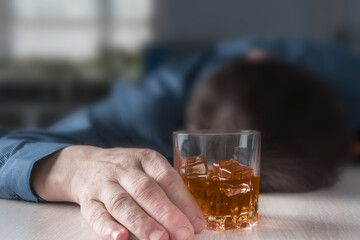 An intoxicated man with a glass of alcohol close-up sleeps unconscious at the table.