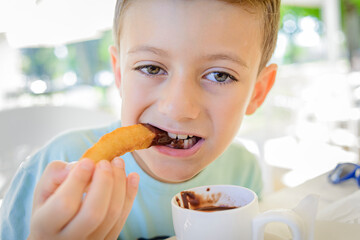 A child eating churros with chocolate.