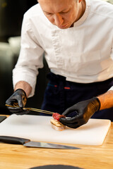 close-up of a chef's hand in black gloves applying a piece of raw cured meat piece of baguette with tweezers