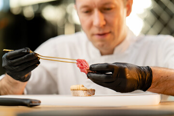 close-up of the face of a chef in black gloves applying a piece of raw cured meat piece of baguette...