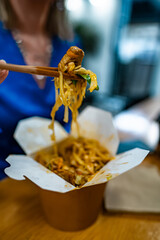 Woman eating noodles with vegetables and meat from Chinese.