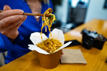 Woman eating noodles with vegetables and meat from Chinese.